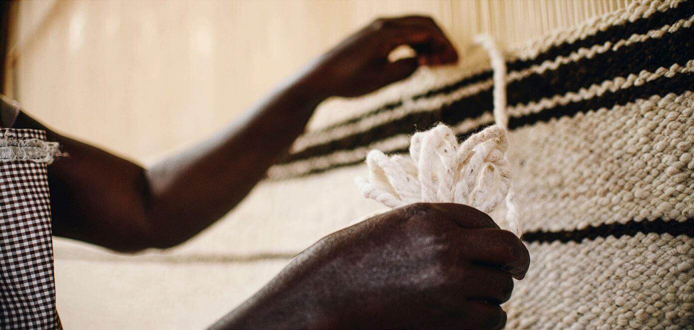 Close-up of the hands of a Sandai weaver carefully inserting threads into a woven pattern with black stripes.