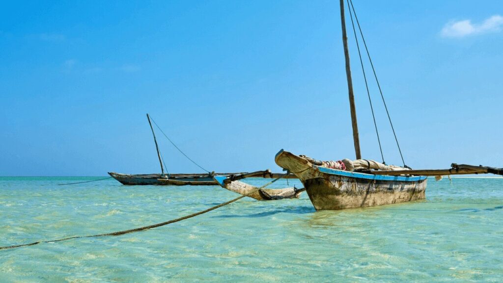 Zwei traditionelle Holzboote mit Segeln, die in klarem, türkisfarbenem Wasser verankert sind, unter einem strahlend blauen Himmel.